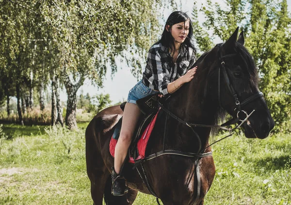 馬会社を楽しんでいる女性 若い美しい女性が黒馬の屋外で遊んだシャツを着て アメリカのカントリースタイルのスタイリッシュな女の子 — ストック写真