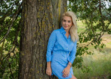 Sweet blonde hair woman in short linen blue color dress at outdoor at natural view clipart