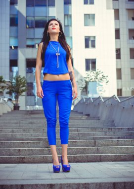 Koyu renk uzun saçlı mavi takım elbiseli bir kadın şehirde arkadaşlarını bekliyor. Büyük bir metropolün ve vatandaşların yaşam tarzı.