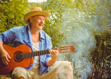 Funny older man in print shirt tourist playing guitar and sing song on nature outdoors, trip to America and pleasure for vacation clipart