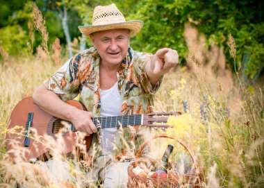 Basılı tişörtlü komik yaşlı adam gitar çalıyor ve doğada şarkı söylüyor, Amerika 'ya seyahat ediyor ve tatil için zevk alıyor.