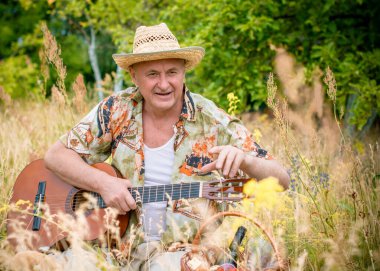 Basılı tişörtlü komik yaşlı adam gitar çalıyor ve doğada şarkı söylüyor, Amerika 'ya seyahat ediyor ve tatil için zevk alıyor.