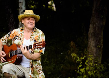 Basılı tişörtlü komik yaşlı adam gitar çalıyor ve doğada şarkı söylüyor, Amerika 'ya seyahat ediyor ve tatil için zevk alıyor.