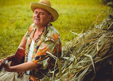 Basılı tişörtlü komik yaşlı adam gitar çalıyor ve doğada şarkı söylüyor, Amerika 'ya seyahat ediyor ve tatil için zevk alıyor.