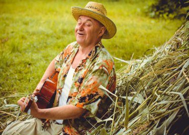 Basılı tişörtlü komik yaşlı adam gitar çalıyor ve doğada şarkı söylüyor, Amerika 'ya seyahat ediyor ve tatil için zevk alıyor.