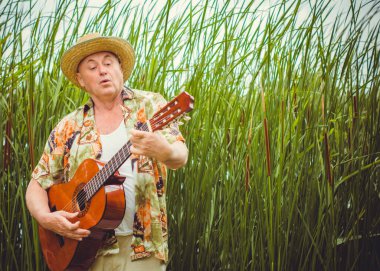 Basılı tişörtlü komik yaşlı adam gitar çalıyor ve doğada şarkı söylüyor, Amerika 'ya seyahat ediyor ve tatil için zevk alıyor.