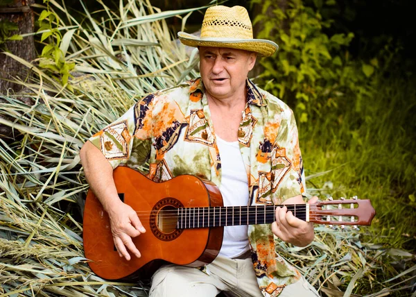 Funny older man in print shirt tourist playing guitar and sing song on nature outdoors, trip to America and pleasure for vacation