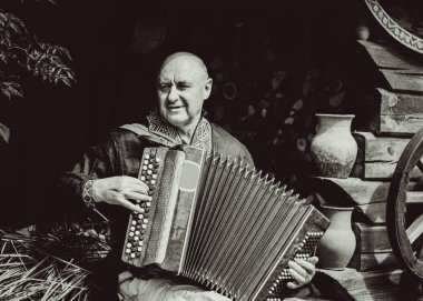 Olgun bir adam müzik aleti akordeonuyla çalar, nakışlı bir gömlek giyer. Slavların yurtdışında birleşmesi