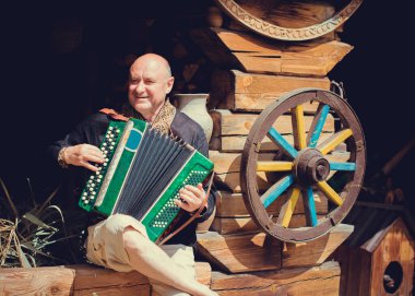 Olgun bir adam müzik aleti akordeonuyla çalar, nakışlı bir gömlek giyer. Slavların yurtdışında birleşmesi