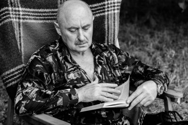 Yaşlı zarif adamın portresi gri saçlı, ekose koltukta kitap okuyor ve hayatını düşünüyor.