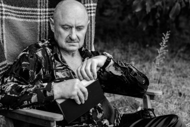 Yaşlı zarif adamın portresi gri saçlı, ekose koltukta kitap okuyor ve hayatını düşünüyor.