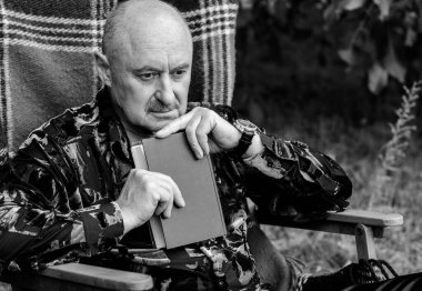 Yaşlı zarif adamın portresi gri saçlı, ekose koltukta kitap okuyor ve hayatını düşünüyor.