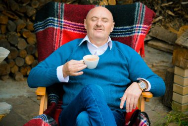 Mavi kazaklı, evde kahve içen olgun bir adam. Hayatın tadını çıkar Zevk Memnuniyet Mutluluk Kavramı