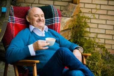 Mavi kazaklı, evde kahve içen olgun bir adam. Hayatın tadını çıkar Zevk Memnuniyet Mutluluk Kavramı