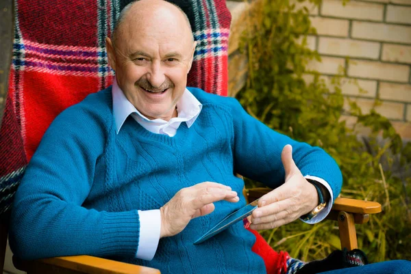 Dijital Tabletli Yaşlı Adam Evdeki Bahçede Kırmızı Ekose Koltukta Oturuyor — Stok fotoğraf