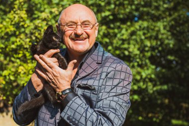 Küçük bir kedisi ve modern emeklilik hayatı olan aktif, kıdemli bir adam. Olgun erkek yaşam tarzı, pozitif duygular, evcil hayvan konsepti.