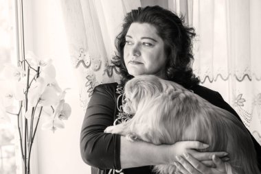 Büyük beden bir bayan ve pencerenin yanında küçük kırmızı yaşlı Pekin köpeği. Bahar zamanı, kutlama.