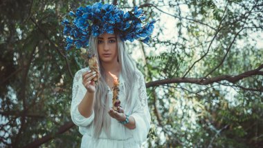 Beautiful girl in wreath of flowers in forest. Portrait of Young beautiful woman wearing white bride dress. Young pagan Slavic girl conduct ceremony on Midsummer. Earth Day