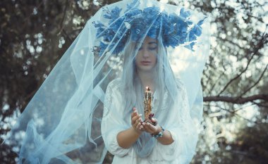 Beautiful girl in wreath of flowers in forest. Portrait of Young beautiful woman wearing white bride dress. Young pagan Slavic girl conduct ceremony on Midsummer. Earth Day