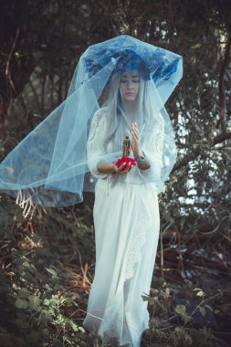 Beautiful girl in wreath of flowers in forest. Portrait of Young beautiful woman wearing white bride dress. Young pagan Slavic girl conduct ceremony on Midsummer. Earth Day