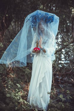 Beautiful girl in wreath of flowers in forest. Portrait of Young beautiful woman wearing white bride dress. Young pagan Slavic girl conduct ceremony on Midsummer. Earth Day