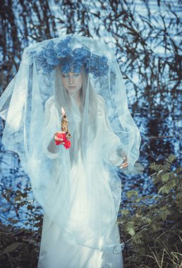 Beautiful girl in wreath of flowers in forest. Portrait of Young beautiful woman wearing white bride dress. Young pagan Slavic girl conduct ceremony on Midsummer. Earth Day