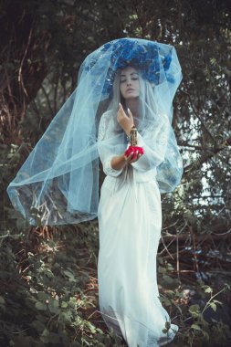 Beautiful girl in wreath of flowers in forest. Portrait of Young beautiful woman wearing white bride dress. Young pagan Slavic girl conduct ceremony on Midsummer. Earth Day