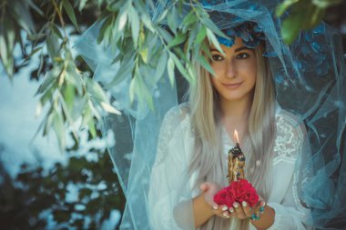 Beautiful girl in wreath of flowers in forest. Portrait of Young beautiful woman wearing white bride dress. Young pagan Slavic girl conduct ceremony on Midsummer. Earth Day