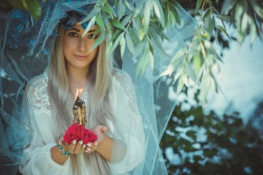 Beautiful girl in wreath of flowers in forest. Portrait of Young beautiful woman wearing white bride dress. Young pagan Slavic girl conduct ceremony on Midsummer. Earth Day