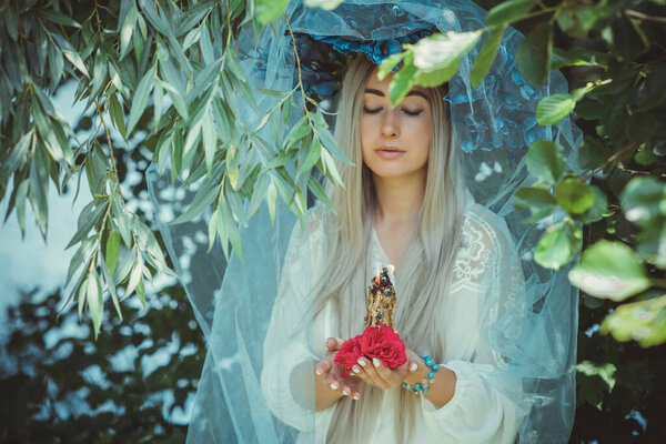 Beautiful girl in wreath of flowers in forest. Portrait of Young beautiful woman wearing white bride dress. Young pagan Slavic girl conduct ceremony on Midsummer. Earth Day