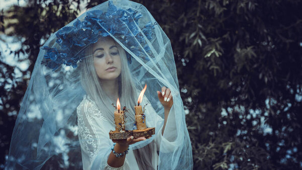 Beautiful girl in wreath of flowers in forest. Portrait of Young beautiful woman wearing white bride dress. Young pagan Slavic girl conduct ceremony on Midsummer. Earth Day