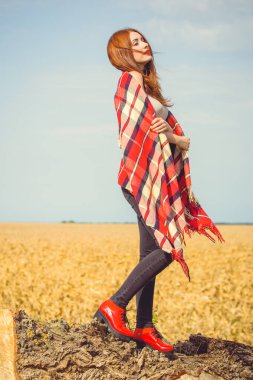 Kırmızı ekoseli, kırmızı ayakkabılı, güneşli sonbahar gününde tarlada dinlenen tatlı kızıl saçlı kız. Şehir kibrinin dışında rahatlık ve uyum kavramı.