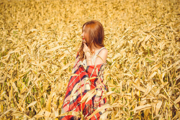Sweet redhead girl in a red checkered plaid, red shoes, resting on the field at sunny warm autumn day. The concept of coziness and harmony outside of city vanity