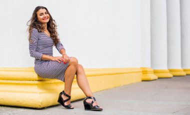 Şehir caddesinde çizgili elbiseli, uzun saçlı, mutlu, Latin bir kızın moda portresi. Olumlu duygular. Yaşam tarzı konsepti, çekici siyah saçlı Arap kadın.