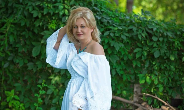  Beyaz elbiseli, dışarıda poz veren, yaşını başını almış olgun bir kadın.