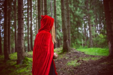 Cadılar Bayramı kavramı. Küçük kırmızı başlıklı güzel ve basit bir kostüm. Sisli ormandaki gizemli kukuletalı figür. Kırmızı yağmurluklu kız. Kostümlü Masal Kırmızı Başlıklı Kız