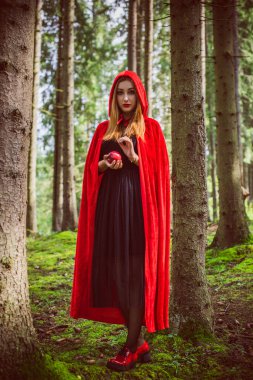 Cadılar Bayramı kavramı. Küçük kırmızı başlıklı güzel ve basit bir kostüm. Sisli ormandaki gizemli kukuletalı figür. Kırmızı yağmurluklu kız. Kostümlü Masal Kırmızı Başlıklı Kız