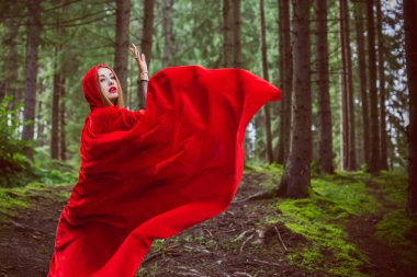 Cadılar Bayramı kavramı. Küçük kırmızı başlıklı güzel ve basit bir kostüm. Sisli ormandaki gizemli kukuletalı figür. Kırmızı yağmurluklu kız. Kostümlü Masal Kırmızı Başlıklı Kız