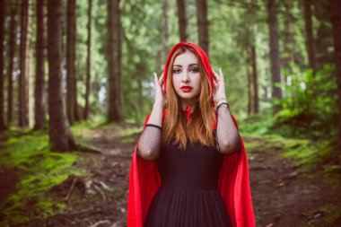 Cadılar Bayramı kavramı. Küçük kırmızı başlıklı güzel ve basit bir kostüm. Sisli ormandaki gizemli kukuletalı figür. Kırmızı yağmurluklu kız. Kostümlü Masal Kırmızı Başlıklı Kız