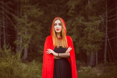 Cadılar Bayramı kavramı. Küçük kırmızı başlıklı güzel ve basit bir kostüm. Sisli ormandaki gizemli kukuletalı figür. Kırmızı yağmurluklu kız. Kostümlü Masal Kırmızı Başlıklı Kız