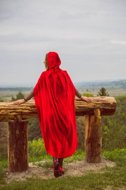 Cadılar Bayramı kavramı. Küçük kırmızı başlıklı güzel ve basit bir kostüm. Sisli ormandaki gizemli kukuletalı figür. Kırmızı yağmurluklu kız. Kostümlü Masal Kırmızı Başlıklı Kız