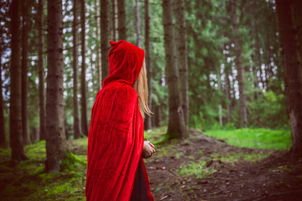Concept of Halloween. Beautiful and simple costume of little red hood. Mysterious hooded figure in misty forest. Girl in red raincoat. Cosplay Fairy Tale Little Red Riding Hood