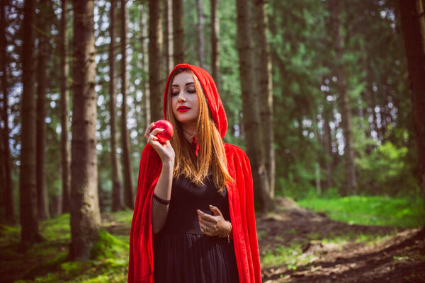 Concept of Halloween. Beautiful and simple costume of little red hood. Mysterious hooded figure in misty forest. Girl in red raincoat. Cosplay Fairy Tale Little Red Riding Hood