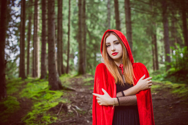 Concept of Halloween. Beautiful and simple costume of little red hood. Mysterious hooded figure in misty forest. Girl in red raincoat. Cosplay Fairy Tale Little Red Riding Hood