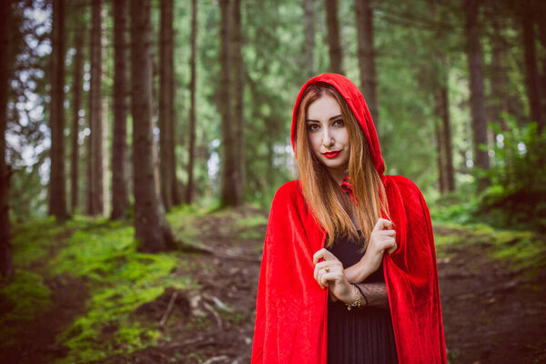 Concept of Halloween. Beautiful and simple costume of little red hood. Mysterious hooded figure in misty forest. Girl in red raincoat. Cosplay Fairy Tale Little Red Riding Hood
