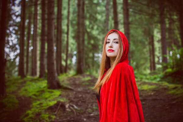 Concept of Halloween. Beautiful and simple costume of little red hood. Mysterious hooded figure in misty forest. Girl in red raincoat. Cosplay Fairy Tale Little Red Riding Hood