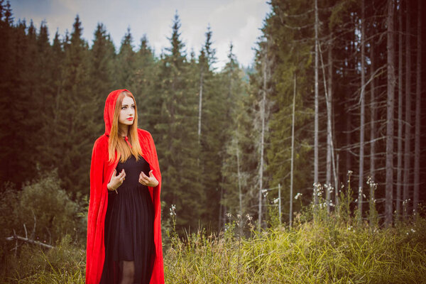 Concept of Halloween. Beautiful and simple costume of little red hood. Mysterious hooded figure in misty forest. Girl in red raincoat. Cosplay Fairy Tale Little Red Riding Hood