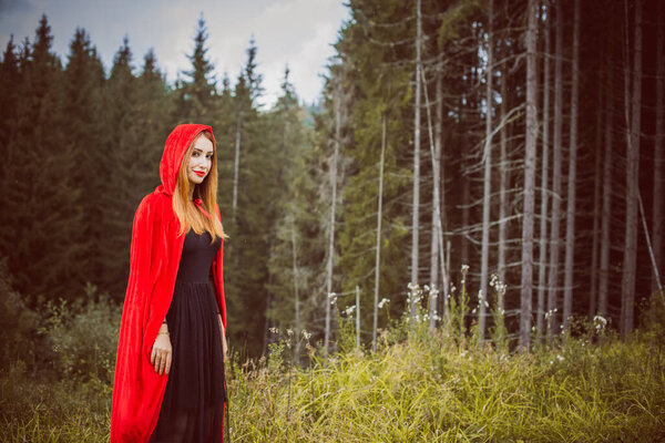Concept of Halloween. Beautiful and simple costume of little red hood. Mysterious hooded figure in misty forest. Girl in red raincoat. Cosplay Fairy Tale Little Red Riding Hood
