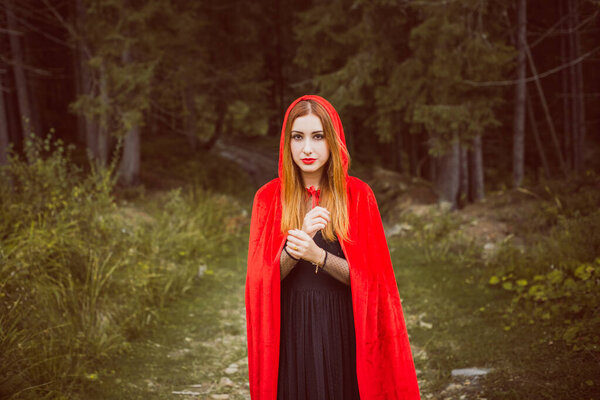 Concept of Halloween. Beautiful and simple costume of little red hood. Mysterious hooded figure in misty forest. Girl in red raincoat. Cosplay Fairy Tale Little Red Riding Hood