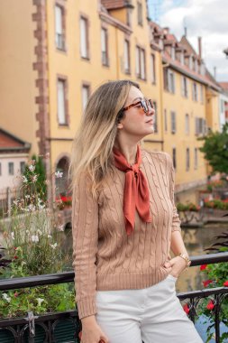 Bej örülü bir kazak, beyaz kot pantolon ve kahverengi ipek eşarp takan bir kadın. Günlük şık kıyafetler Fransız caddesinde moda ve yaşam tarzı için mükemmel.